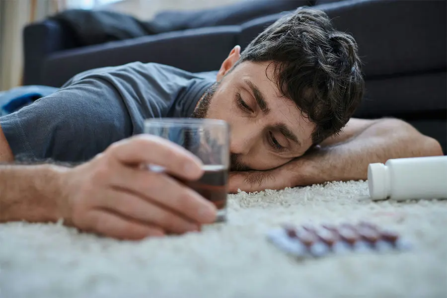 Man lying on the floor holding alcohol, with a bottle and packet of substance nearby