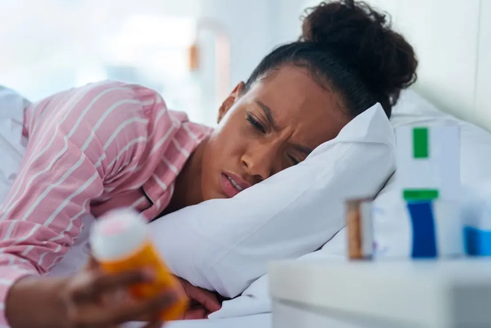 a women laying on bed while holding a bottle of pills